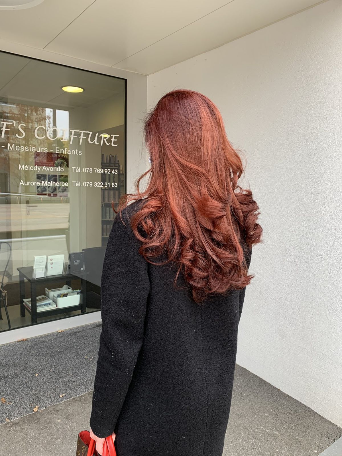 Une cliente aux cheveux cuivrés devant la vitrine du salon