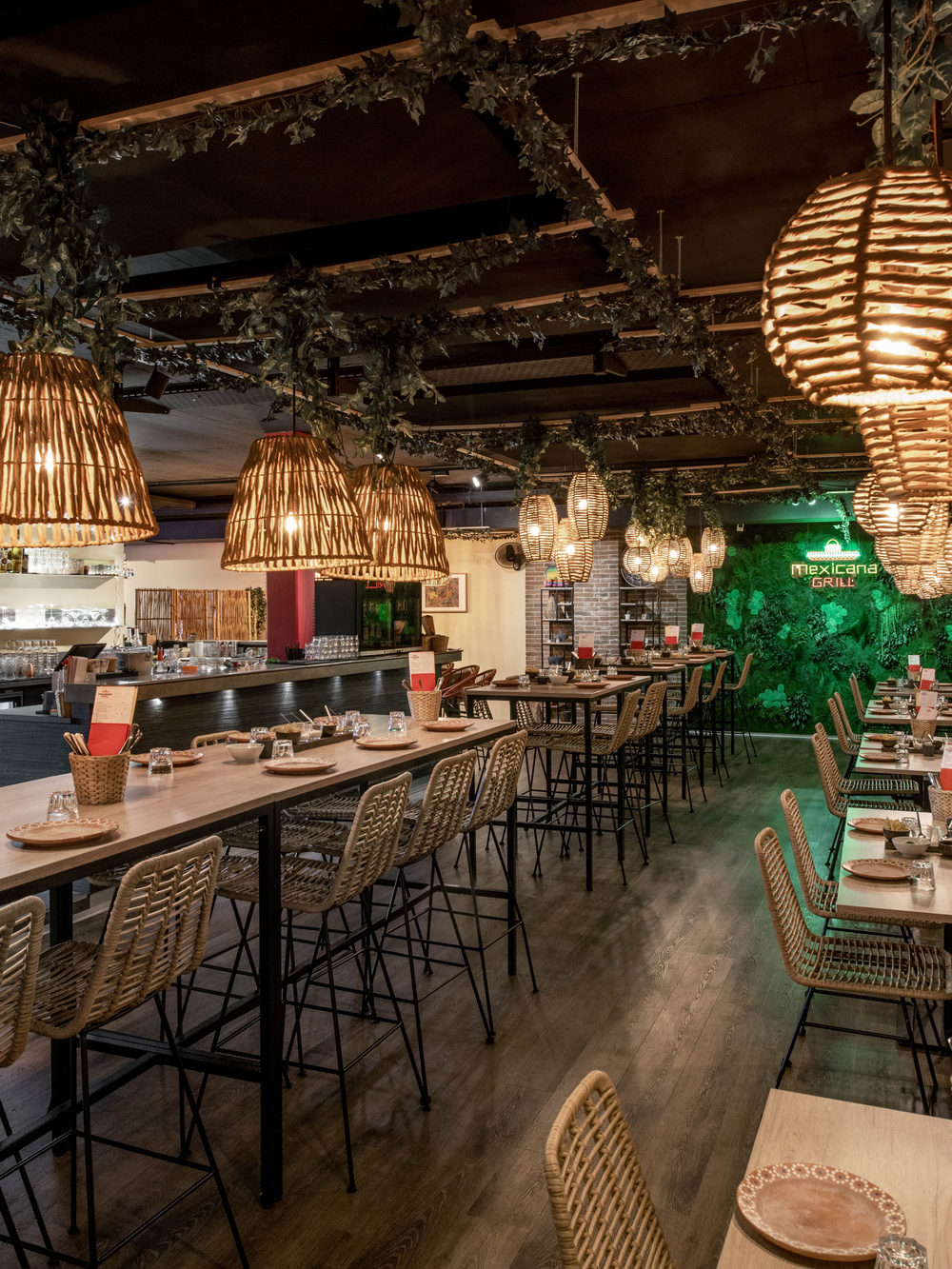La salle du restaurant, tables hautes sous les lampes en osier, enseigne lumineuse sur le mur végétal