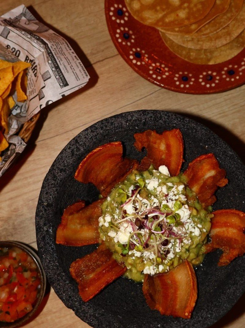Guacamole im Molcajete serviert, mit Chicharrón und Tortillas